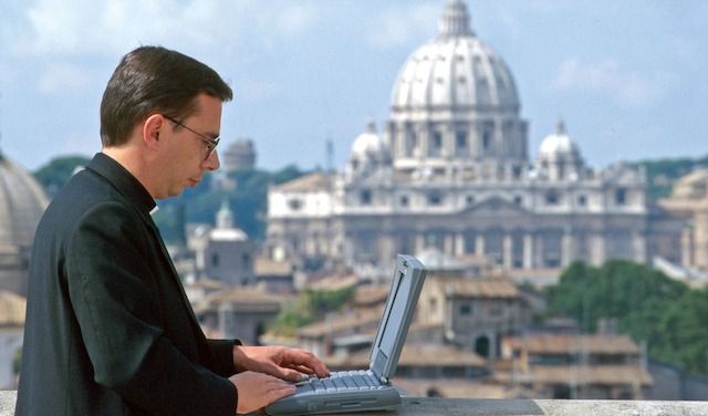 UN SACERDOTE AL LAVORO CON IL COMPUTER PORTATILE
