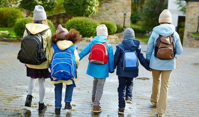 Schoolkids in casualwear with rucksacks behind backs holding by hands while going to school