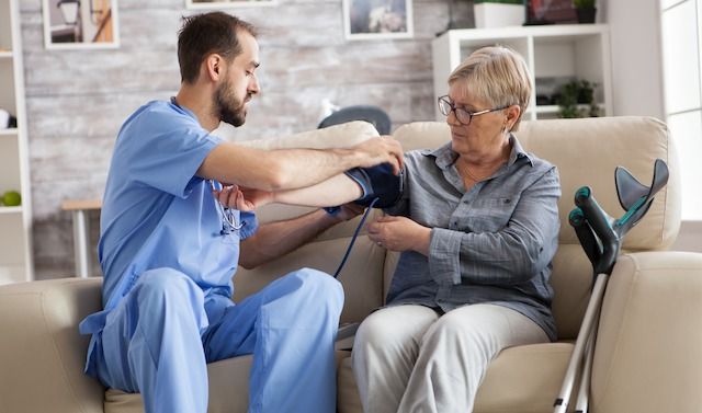 Male nurse with old woman on couch in nursing home using blood pressure meter.