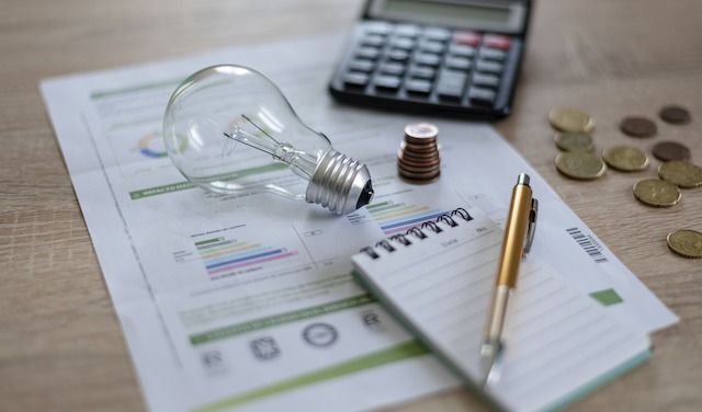 Light bulb with coins, notebook with a pen and calculator and light bill on a wooden background