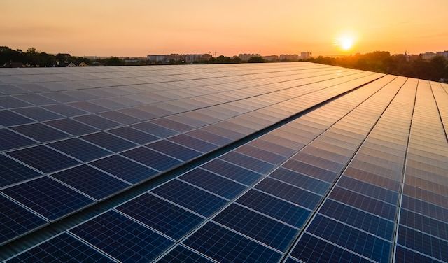 Blue photovoltaic solar panels mounted on building roof for producing clean ecological electricity at sunset. Production of renewable energy concept.